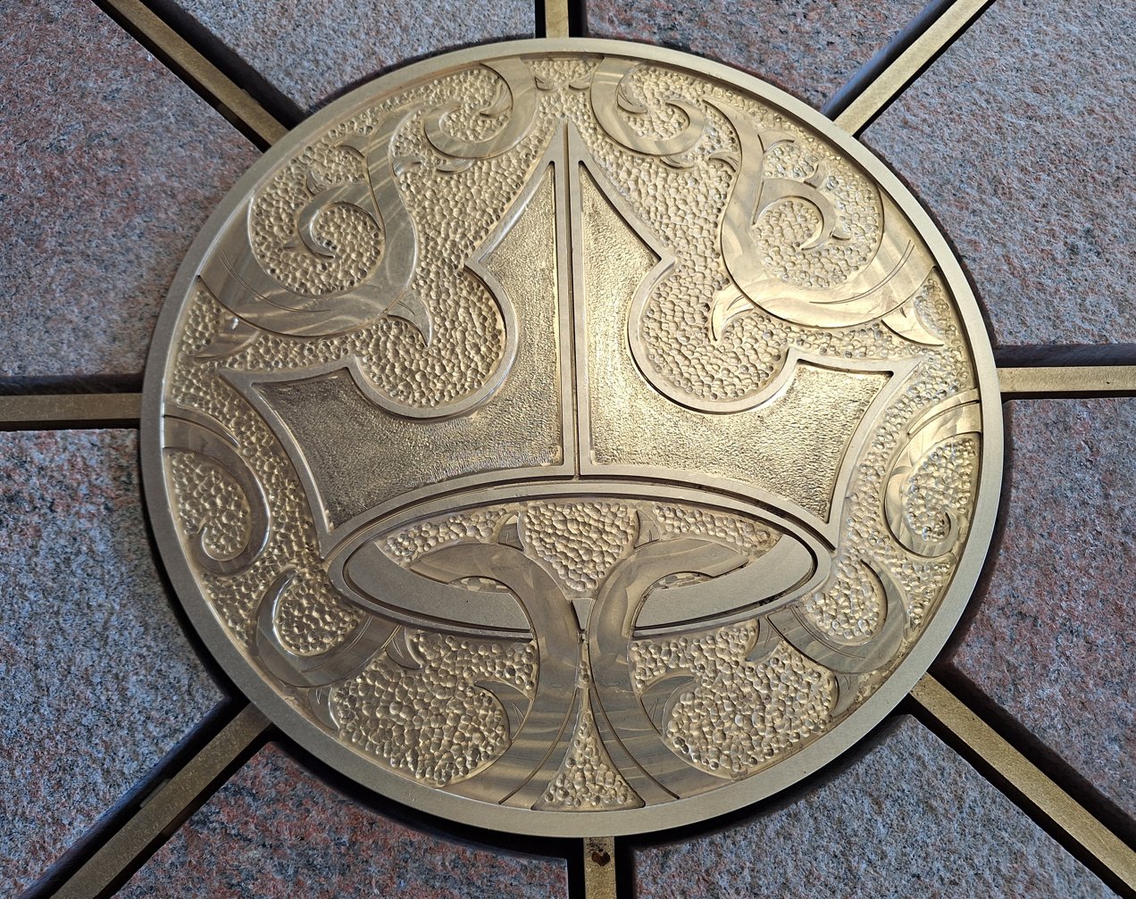 Close-up of a brass medallion showing a crown surrounded by thorny scrollwork