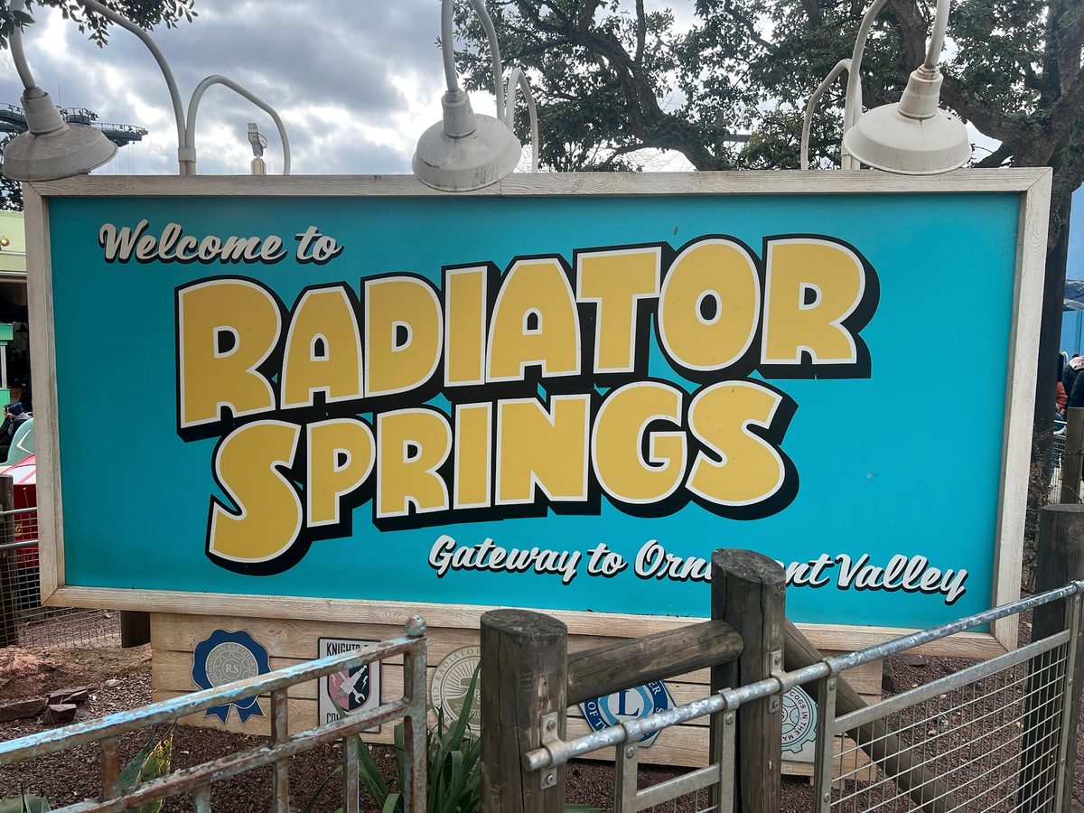 The turquoise Welcome to Radiator Springs sign under a row of lamps in Worlds of Pixar