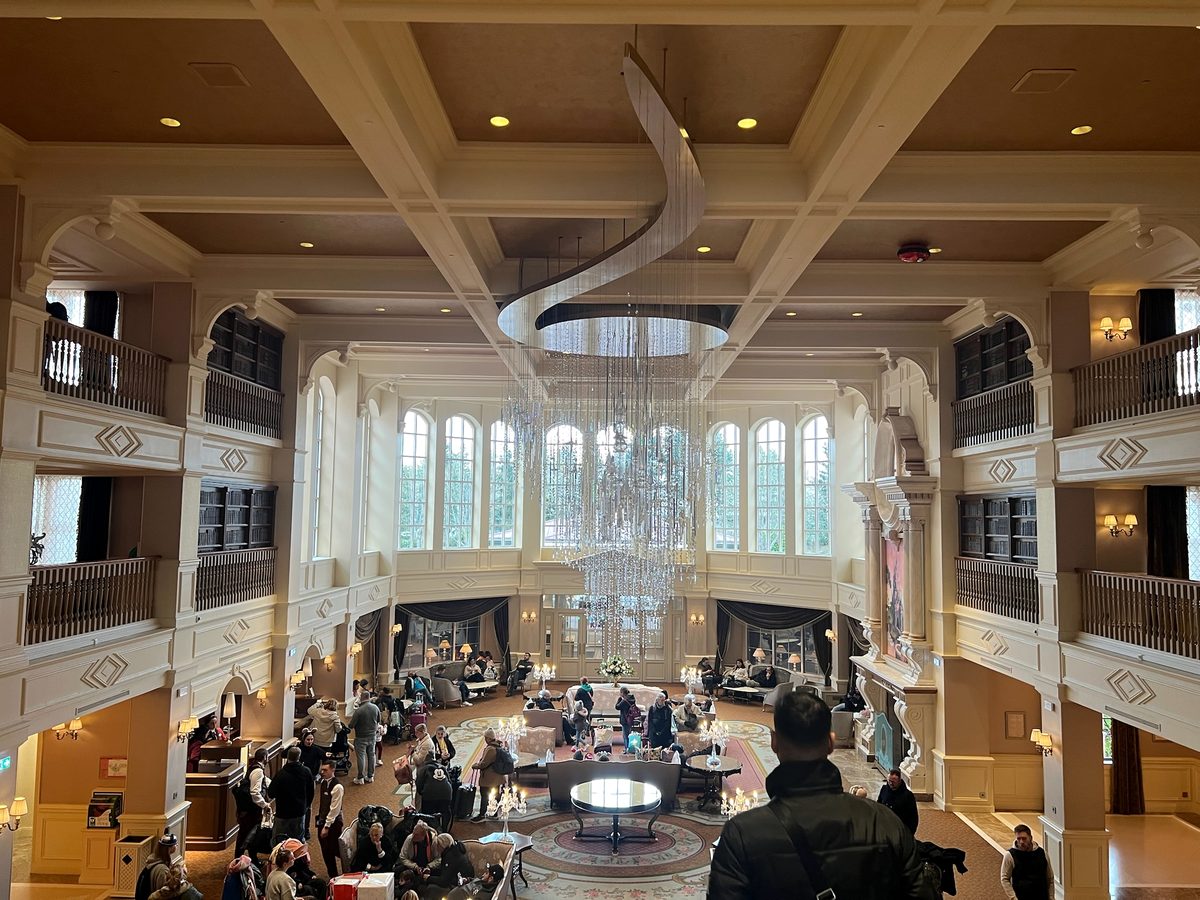 The Disneyland Hotel lobby seen from the mezzanine, a long crystal chandelier over the seating with tall arched windows behind