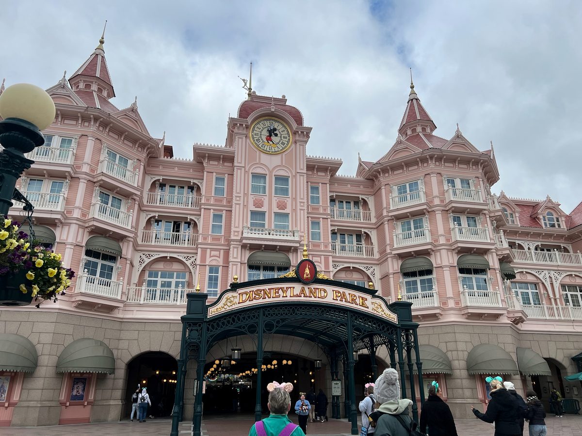 Guests walking beneath the pink facade of the Disneyland Hotel and under the Disneyland Park entrance arch