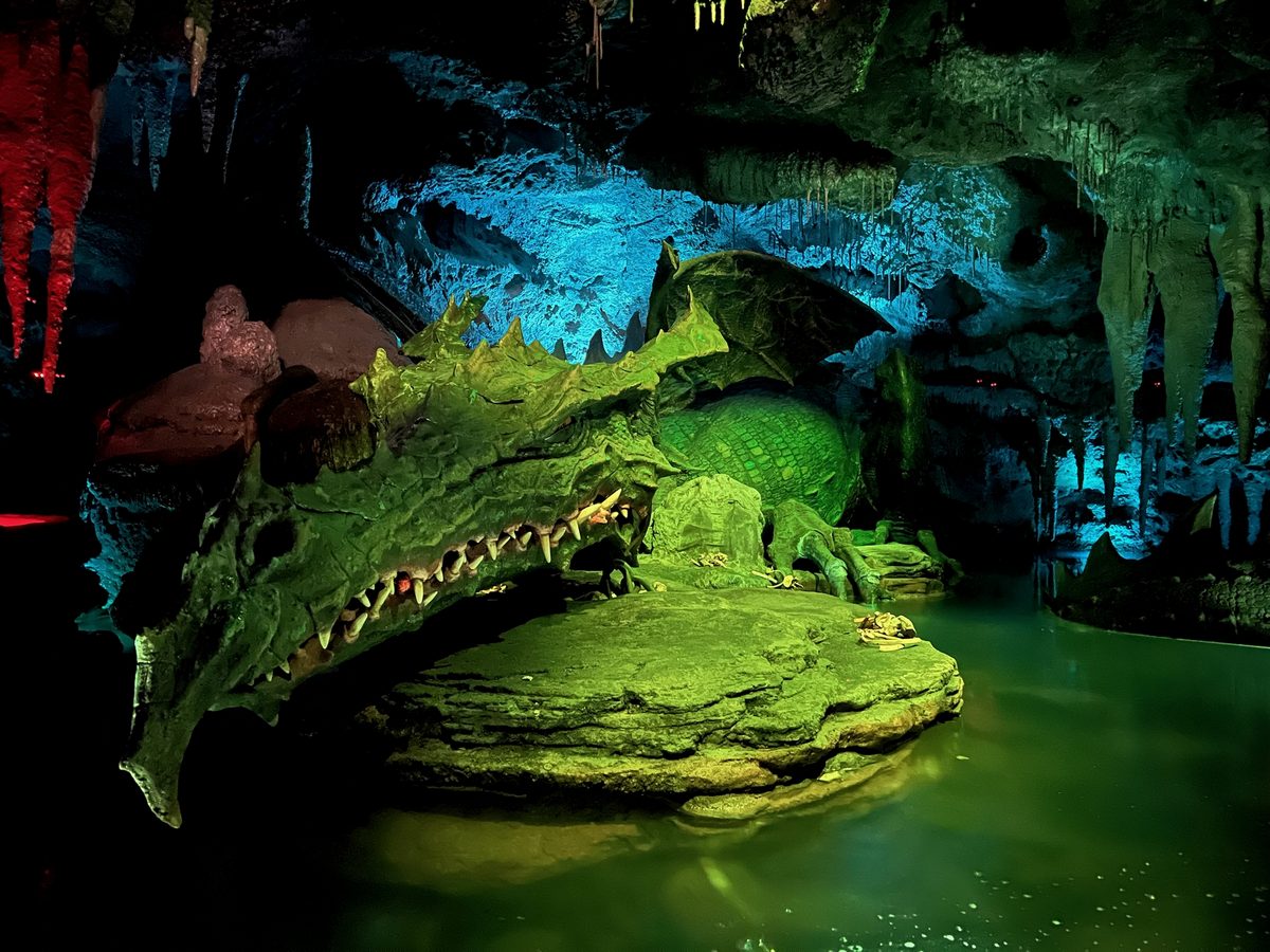 The animatronic dragon resting on a rock in the green-lit cavern of La Tanière du Dragon
