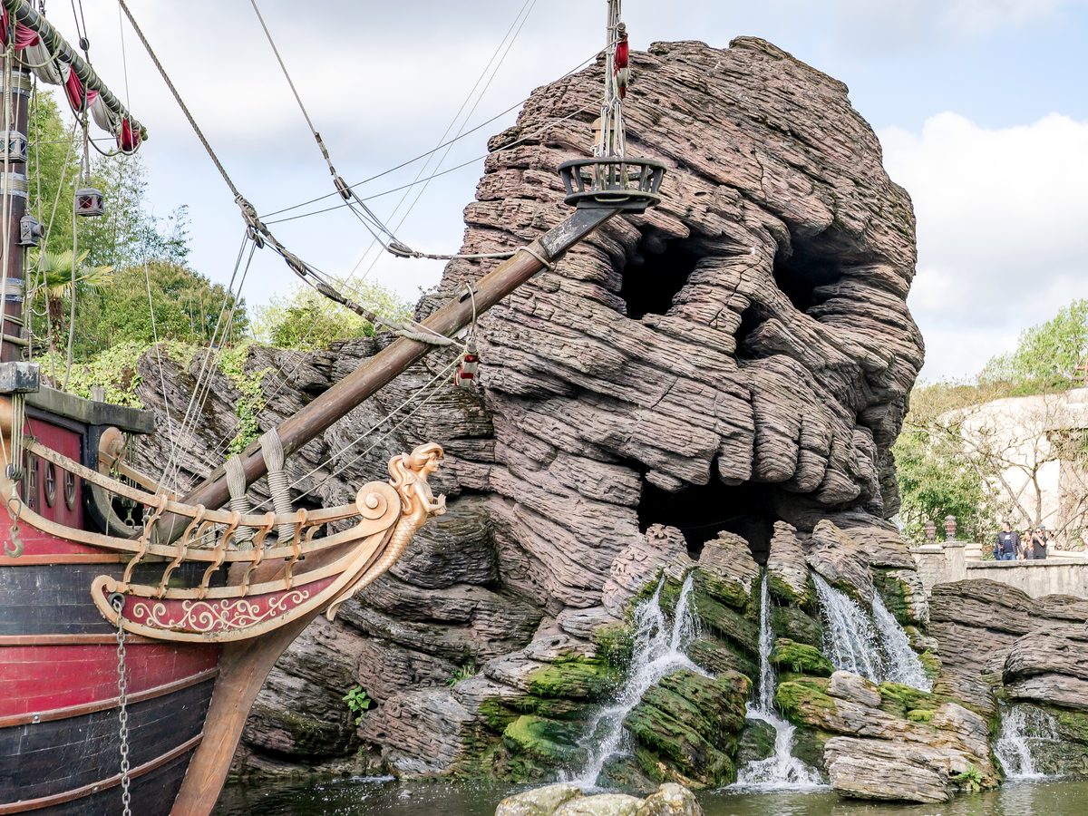 Skull Rock, a skull-shaped rock formation with waterfalls spilling below it, beside the bow of a pirate ship on Adventure Isle