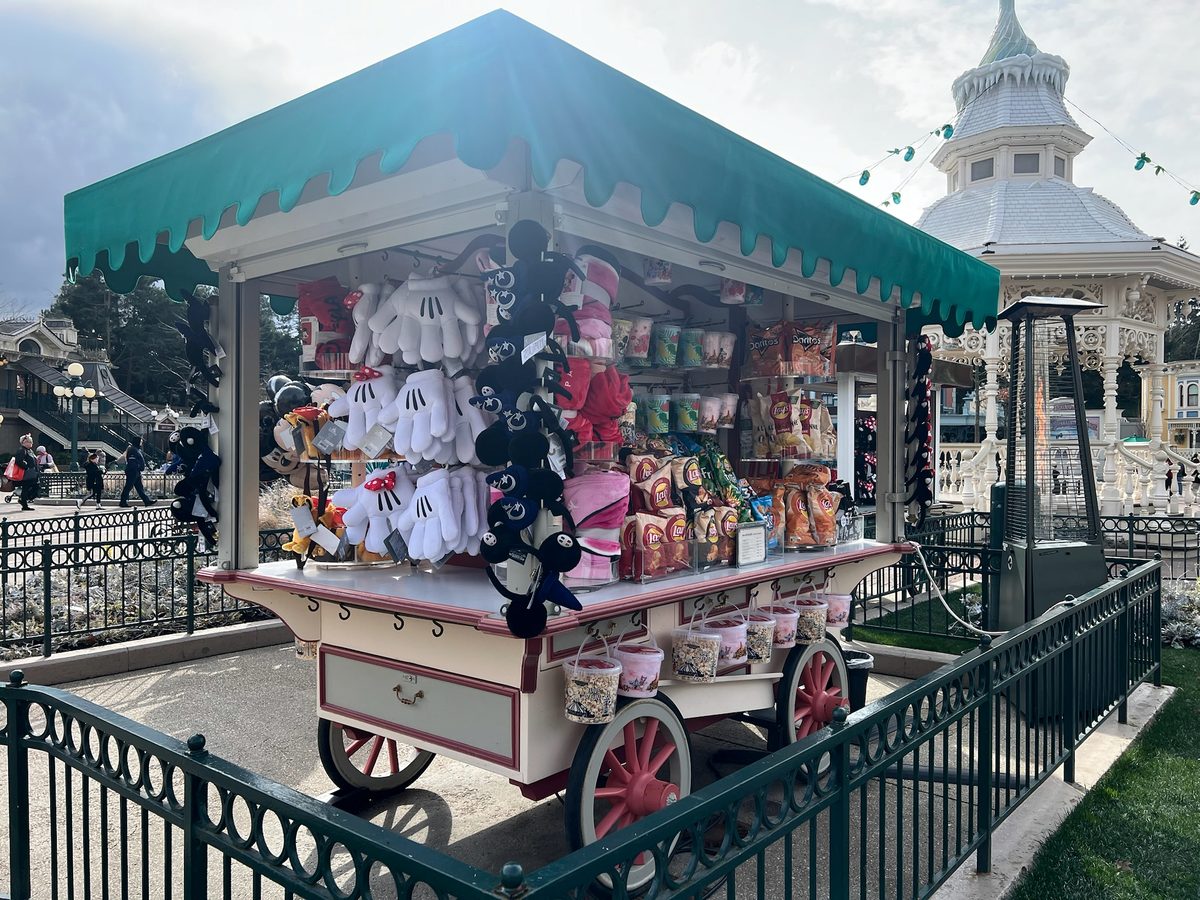 A souvenir cart under a green canopy, stocked with plush toys, Mickey gloves and popcorn buckets