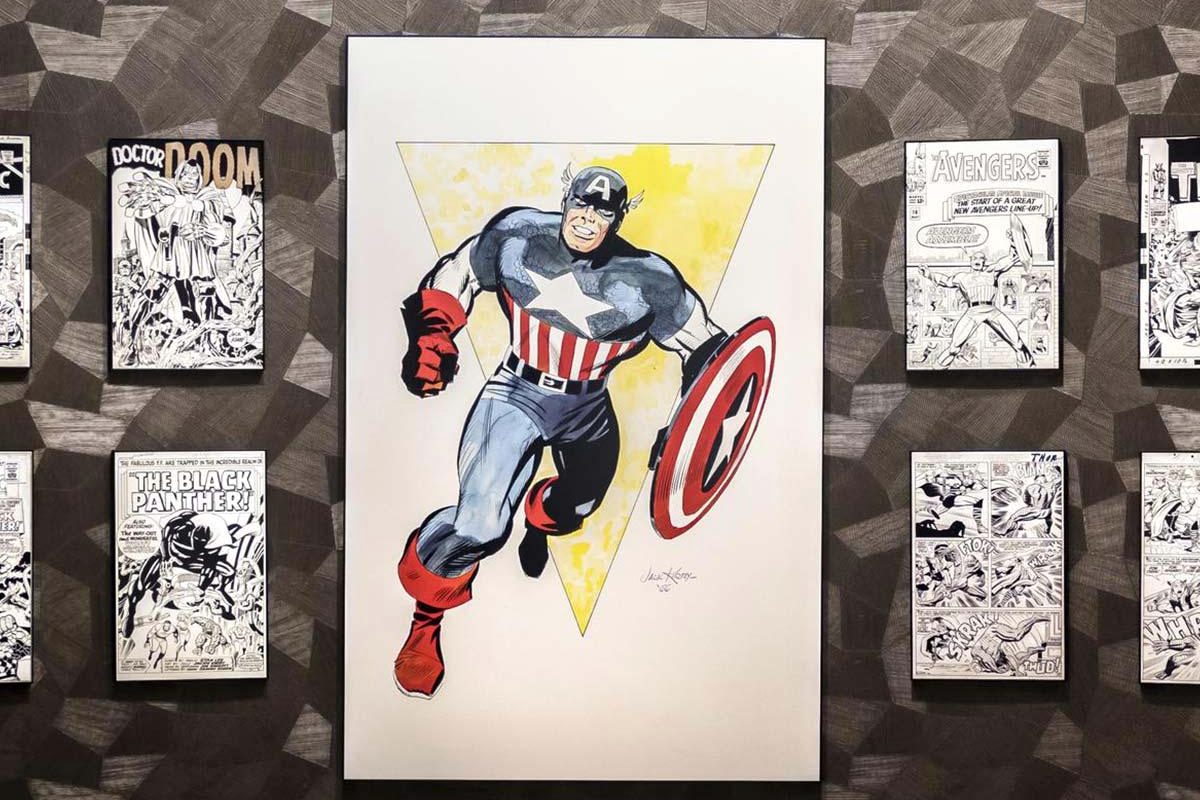 A large painted Captain America canvas on a patterned wall, flanked by framed vintage Marvel comic covers including Doctor Doom, Black Panther, Avengers and Thor