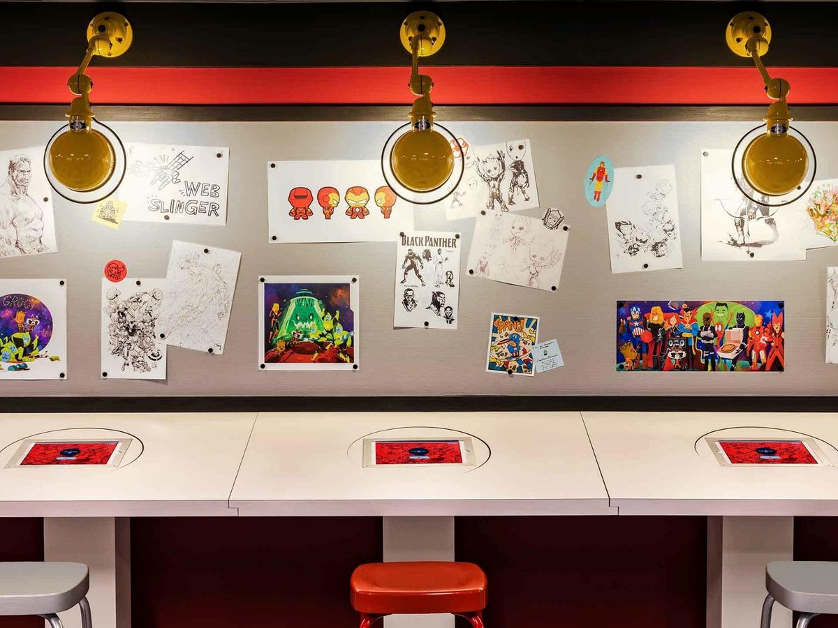 The Marvel Design Studio, white desks with tablets set into them beneath a wall pinned with character sketches and artwork