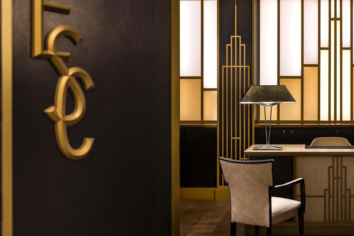The Empire State Club, a gold ESC monogram on a dark wall beside a gold art-deco screen and a lamp on a desk