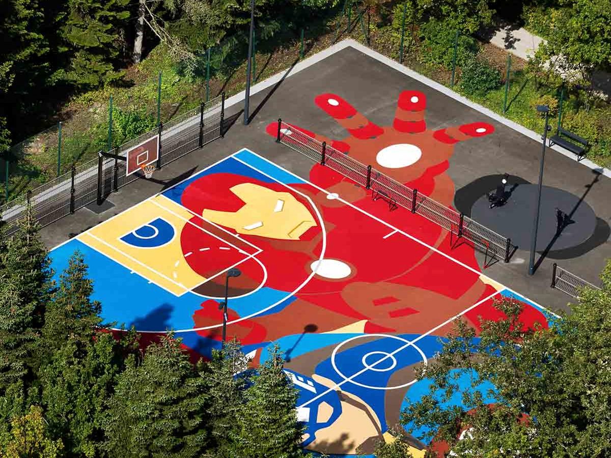 The Hero Training Zone from above, a basketball and sports court painted with a giant Iron Man, set among trees
