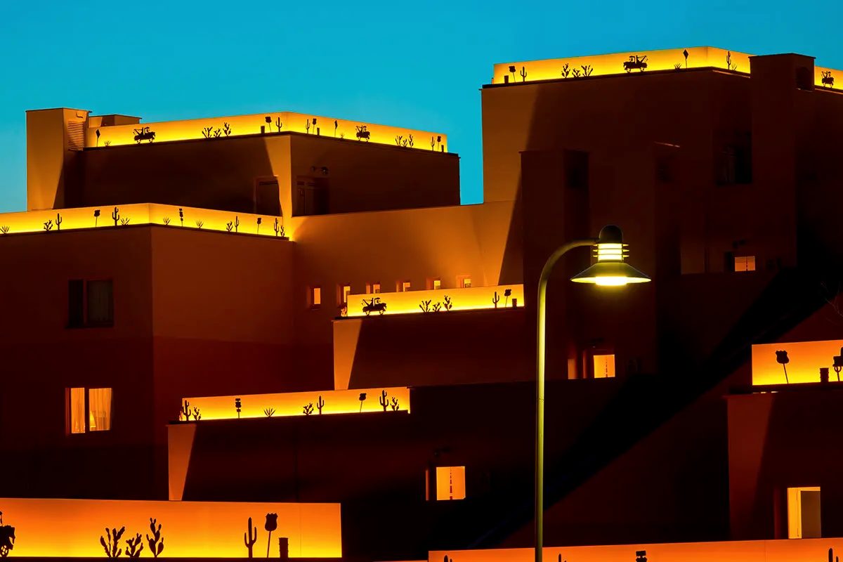 The tiered adobe blocks of Disney's Hotel Santa Fe glowing at dusk, Route 66 cactus and pickup-truck light strips along each roofline against a deep blue sky
