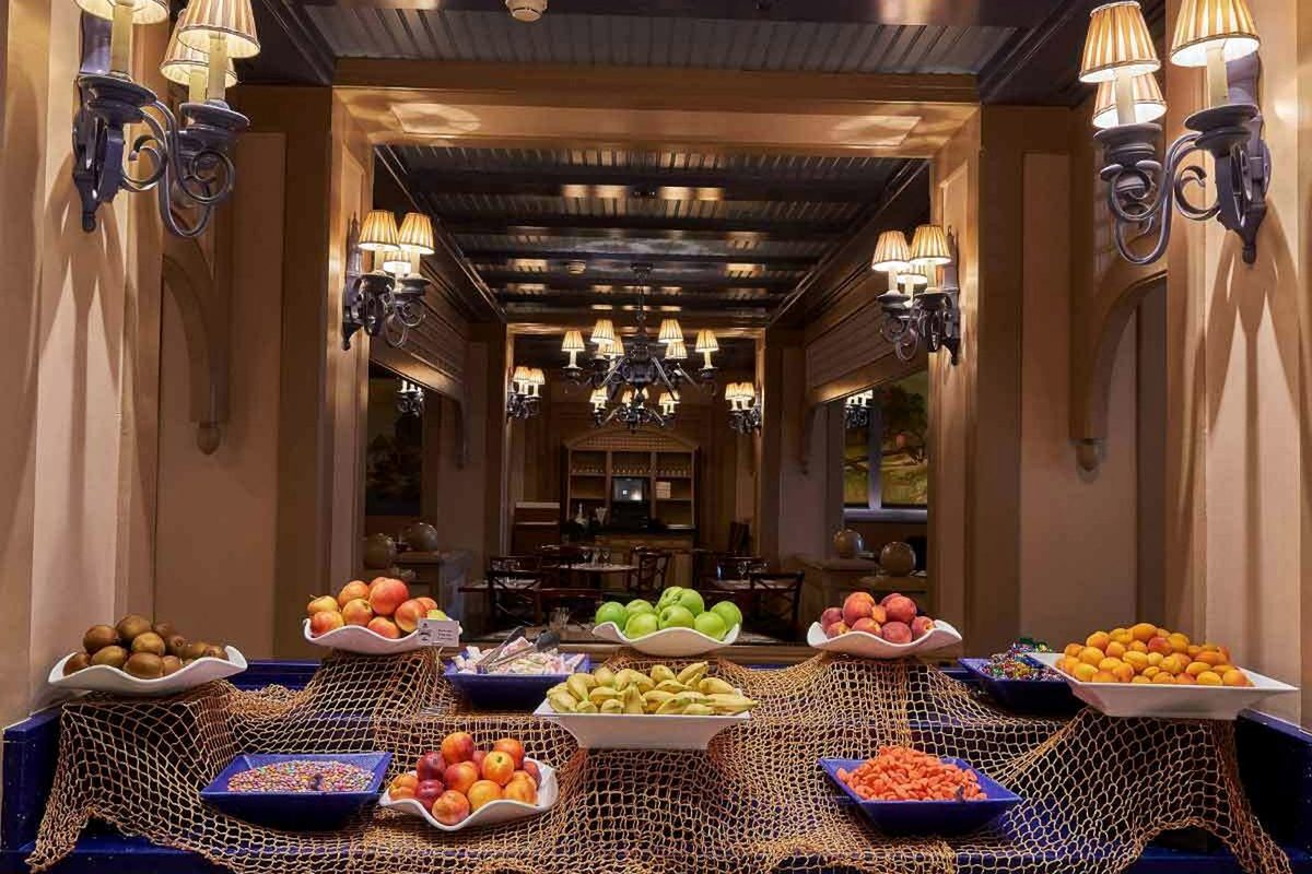 The fruit table at the Cape Cod buffet, bowls of apples, pears, apricots and kiwi on a counter draped in fishing net under wrought-iron candelabra