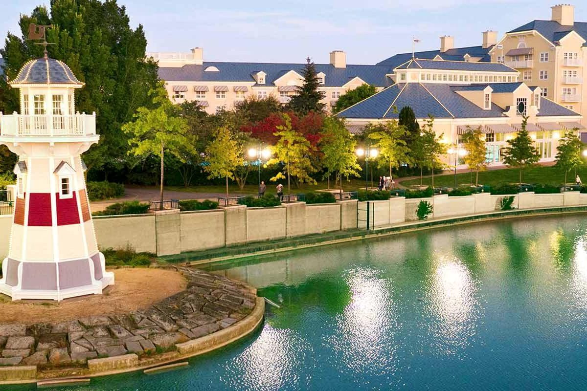 The Harbour Light, the hotel's white-and-red lighthouse, standing on the shore of Lake Disney with the crescent hotel behind and autumn trees around