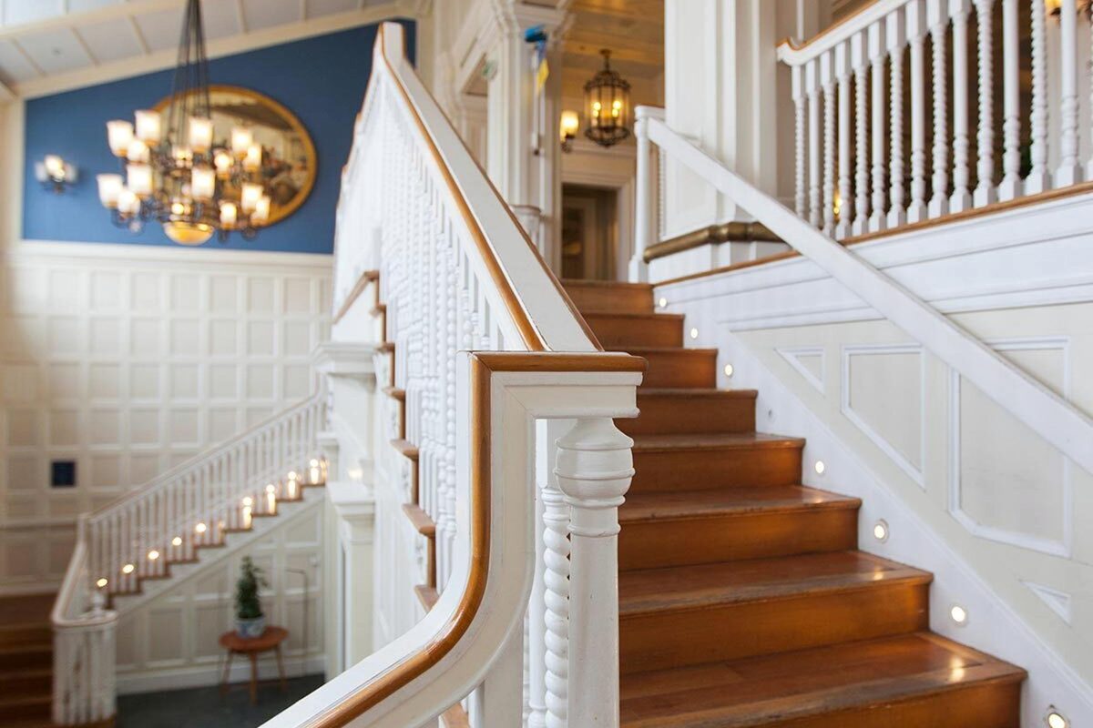 The main staircase in the lobby of Disney Newport Bay Club, white balustrades and wooden treads beneath a chandelier, with a blue panelled wall and an oval framed painting behind