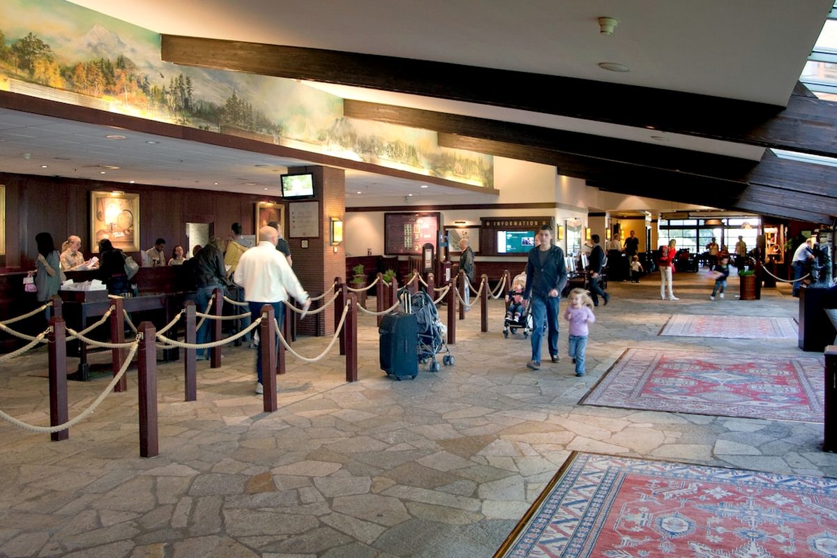 The lobby at Disney Sequoia Lodge, a flagstone floor beneath a painted forest-and-mountain mural, with the check-in desks along one side and a family crossing with a pram