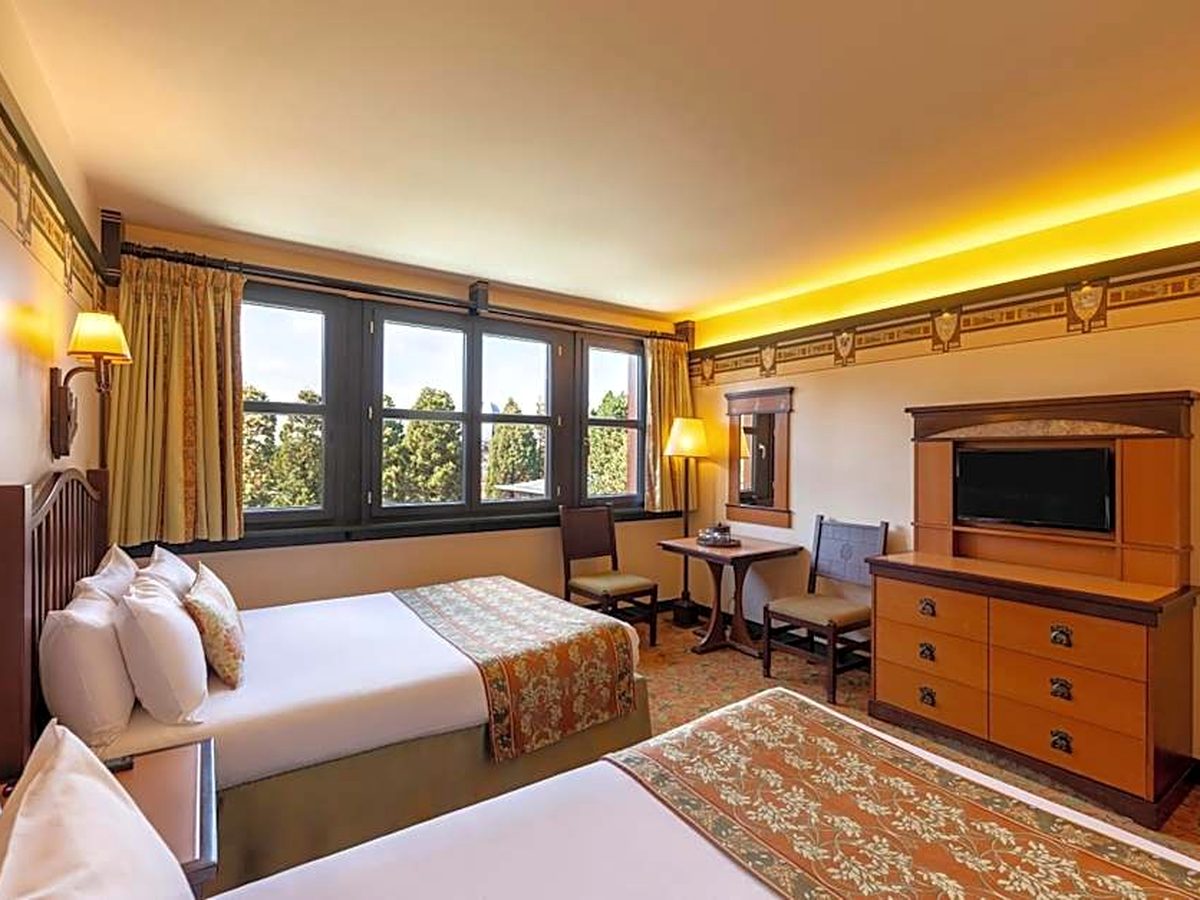 A standard room at Disney Sequoia Lodge with two beds, a timber dresser and a television cabinet