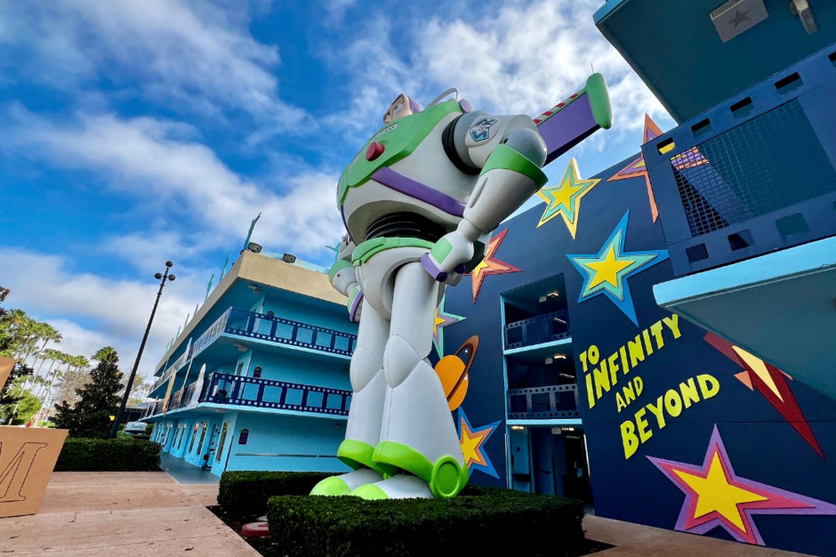 A giant Buzz Lightyear figure standing over the hedges of the Toy Story courtyard at Disney All-Star Movies, beside a dark-blue building painted with stars and the words To Infinity and Beyond