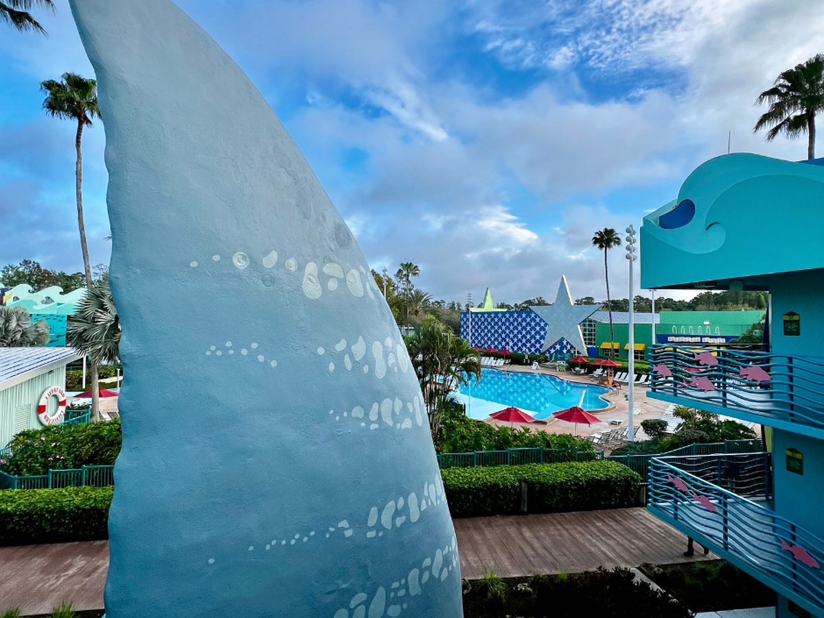 Surfboard Bay, the main pool at Disney All-Star Sports, seen past a giant shark fin, with red parasols and a white star at the far end