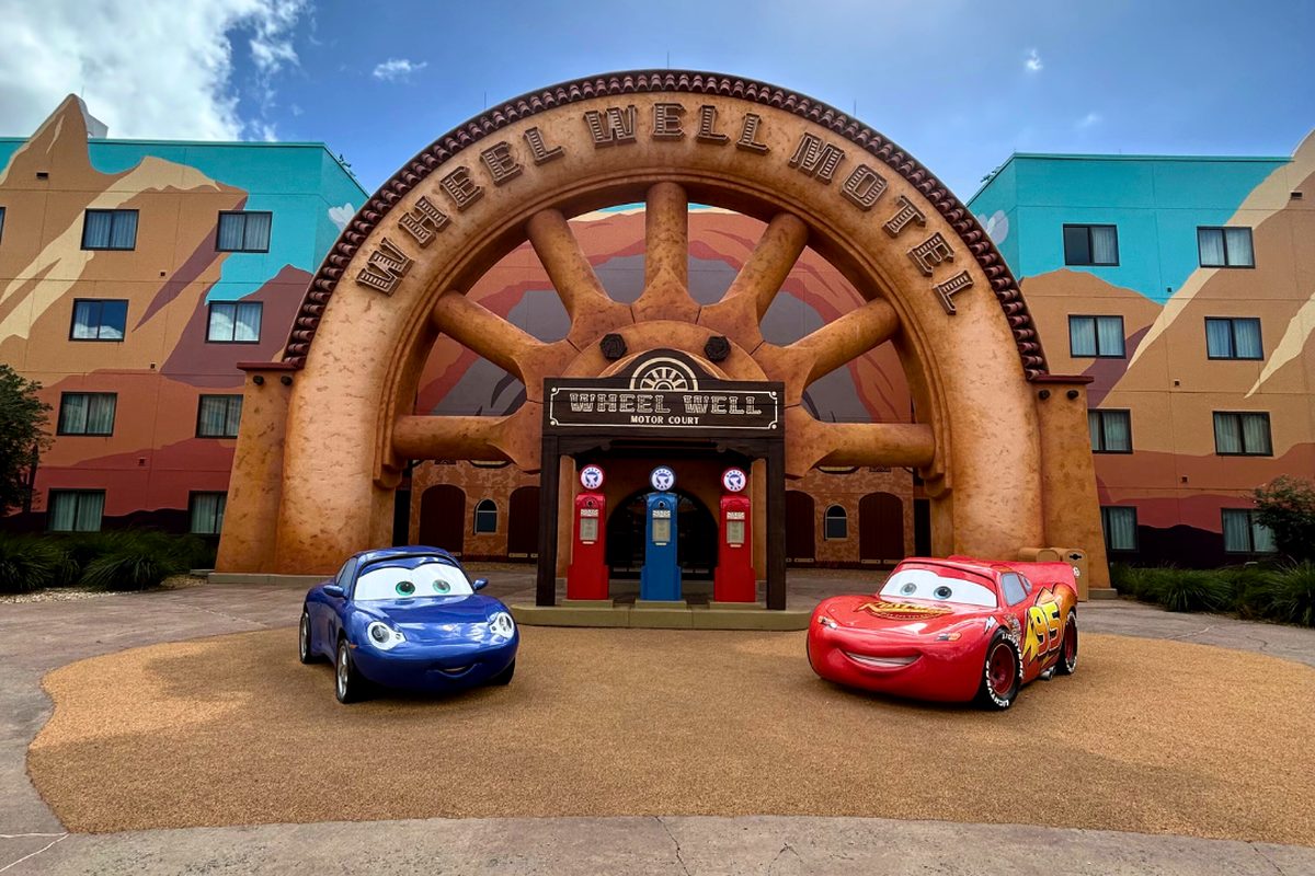 Sally and Lightning McQueen statues in front of the Wheel Well Motel arch, with a painted Radiator Springs desert on the buildings behind, in the Cars courtyard at Art of Animation