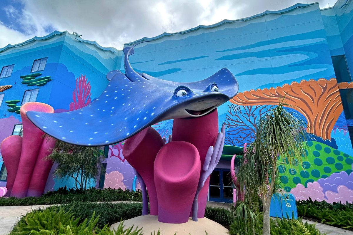 A giant statue of Mr Ray the spotted stingray on pink coral, against a building painted as an underwater reef, in the Finding Nemo courtyard at Art of Animation