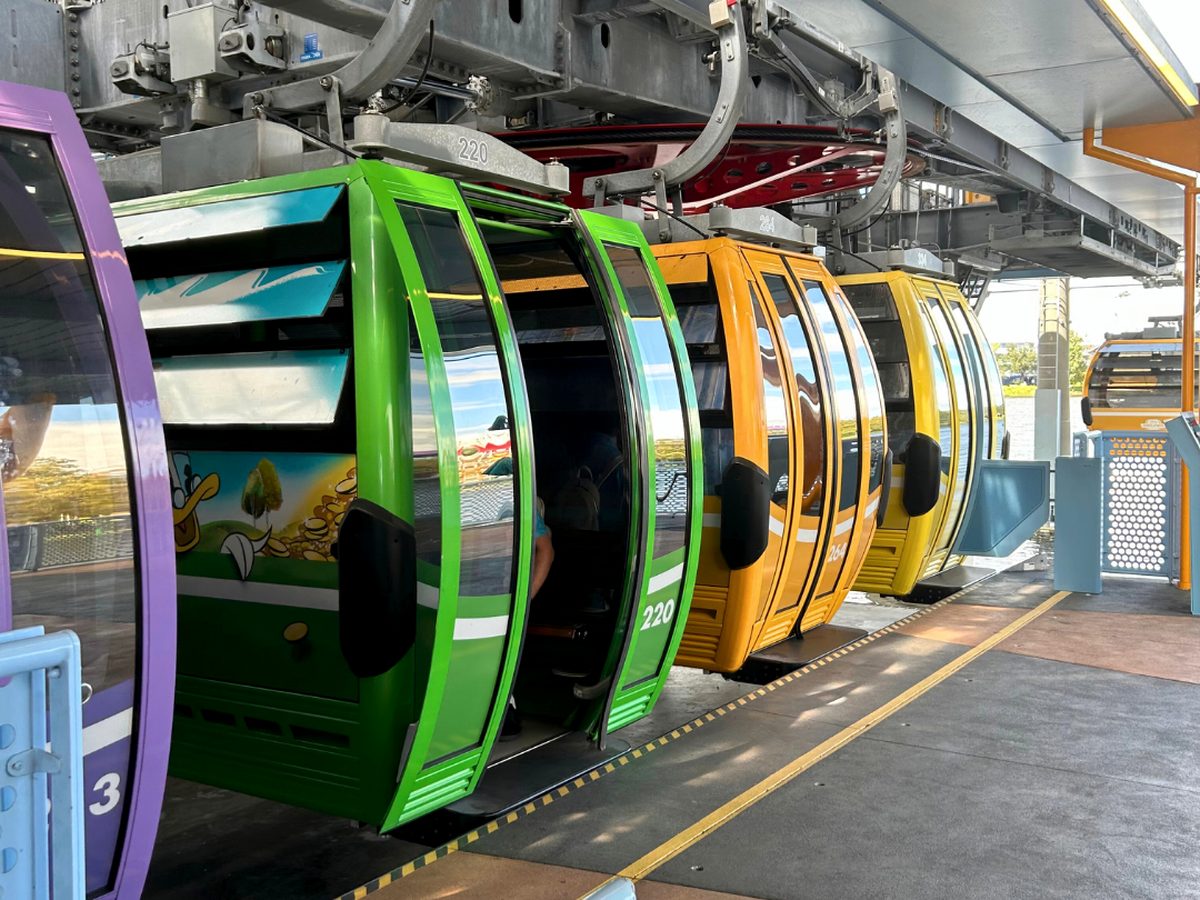 Green, orange and yellow Disney Skyliner gondolas lined up at the loading platform inside the resort station