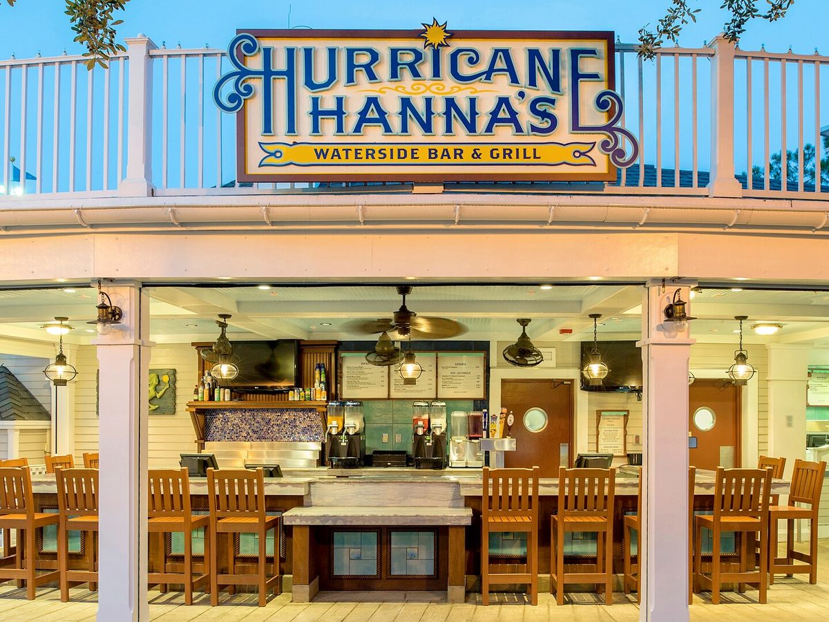 The open-air counter of Hurricane Hanna's Waterside Bar & Grill, wooden stools under its painted sign