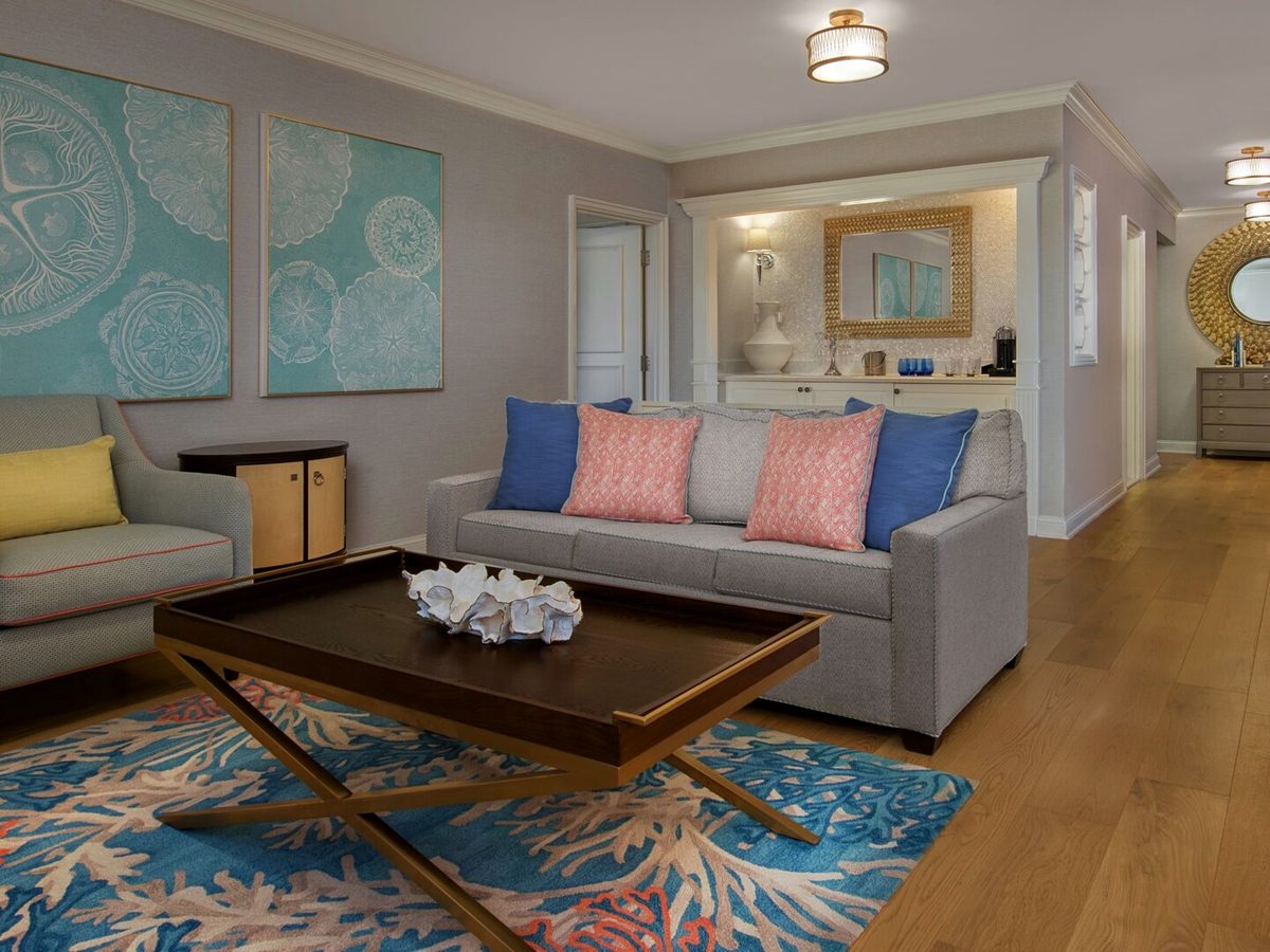 A Beach Club Villas living room with a grey sofa, coral and blue cushions and a coral-patterned rug
