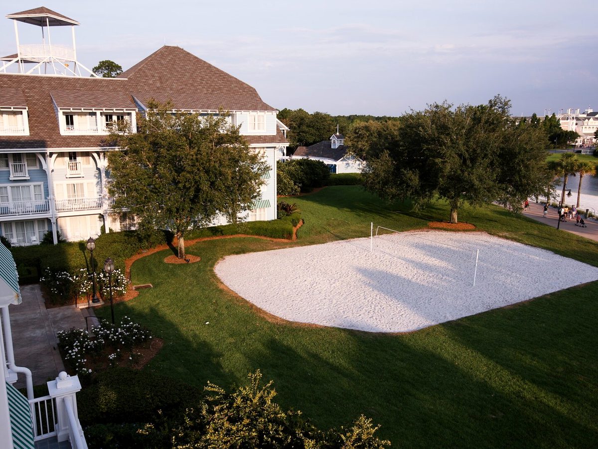 The sand volleyball court beside the Beach Club buildings, seen from a balcony above with Crescent Lake beyond