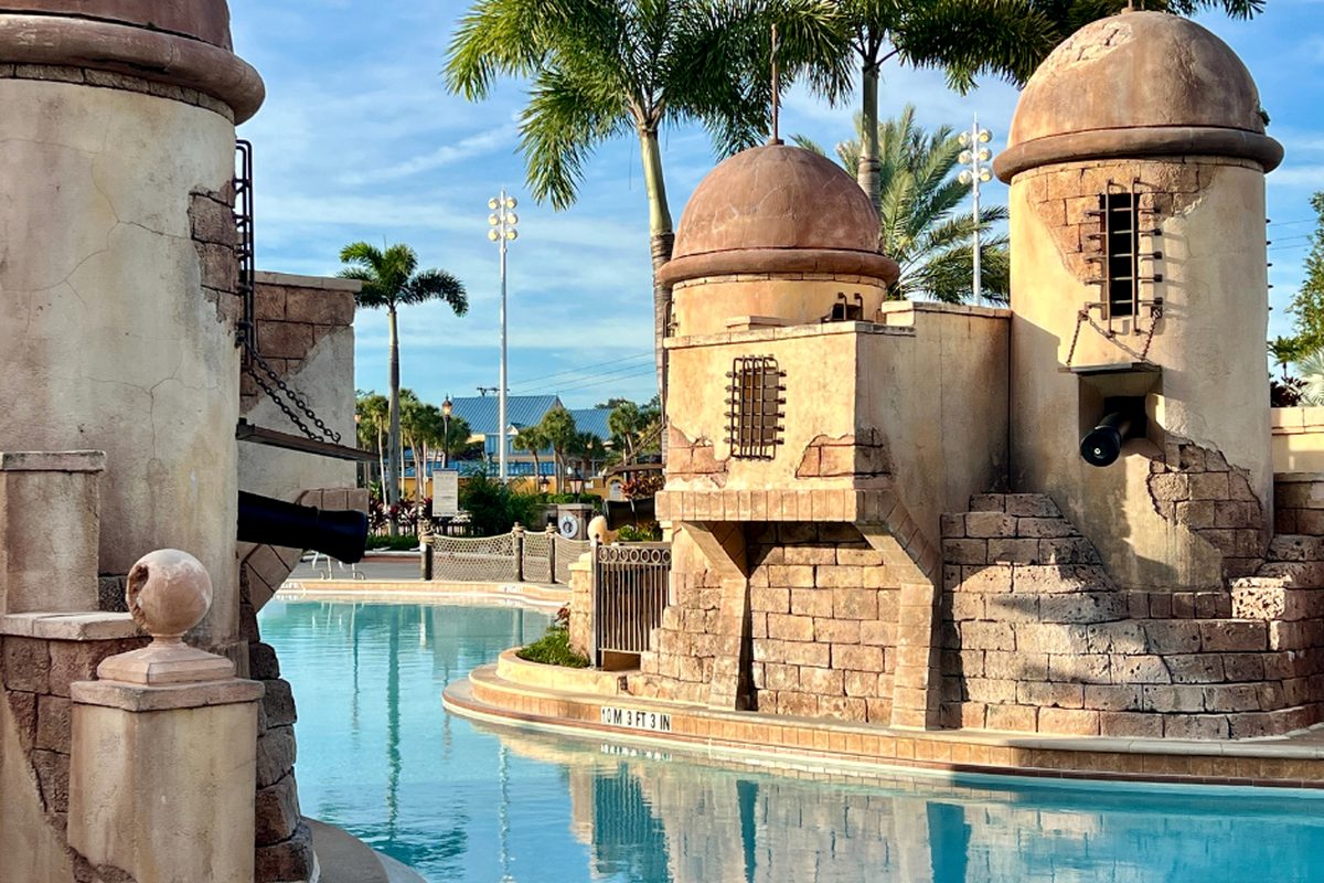 The stone turrets and cannons of Fuentes del Morro, the fort-themed feature pool at Disney's Caribbean Beach Resort, with palm trees behind