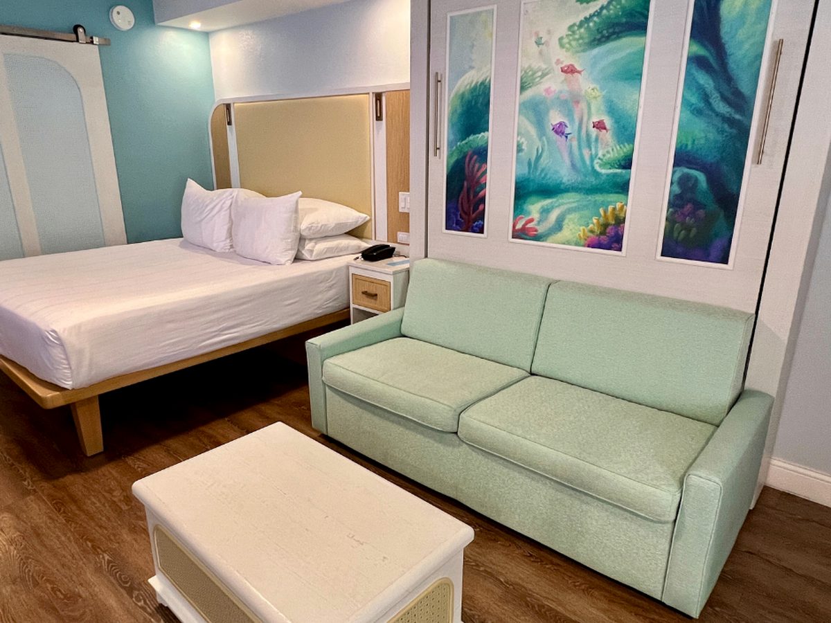 A Little Mermaid room at Disney's Caribbean Beach Resort, the sofa beneath an underwater mural on the stowed fold-away queen, with the raised queen bed beyond