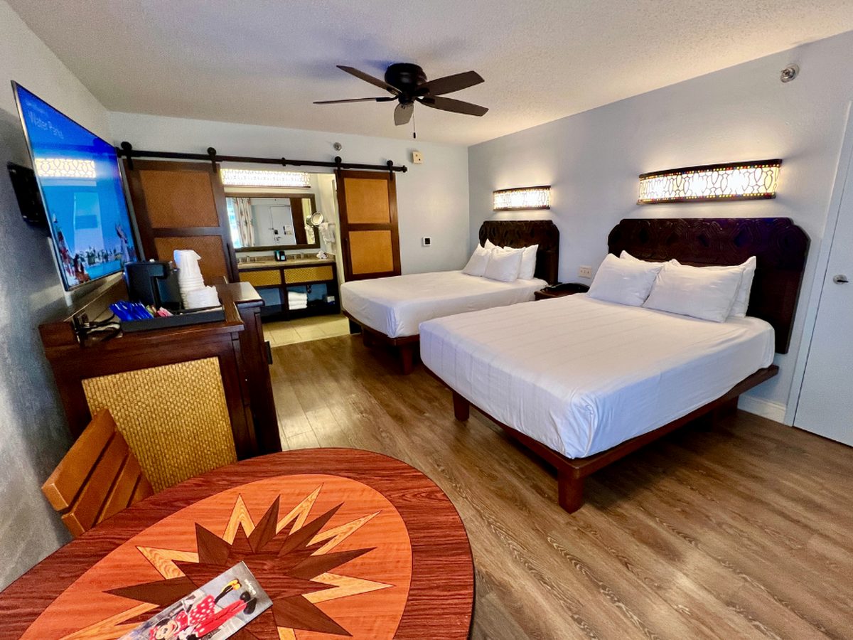 A standard room at Disney's Caribbean Beach Resort with two queen beds, dark wood headboards and a compass-rose table in the foreground