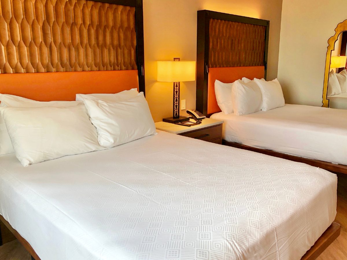 A Gran Destino Tower room at Disney's Coronado Springs Resort, two queen beds with carved-wood and orange leather headboards and a lamp between them