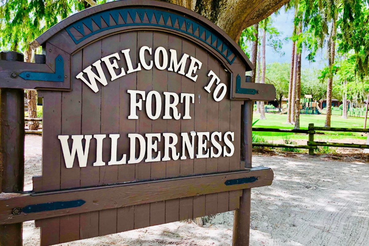 The wooden 'Welcome to Fort Wilderness' sign among tall trees at the resort entrance
