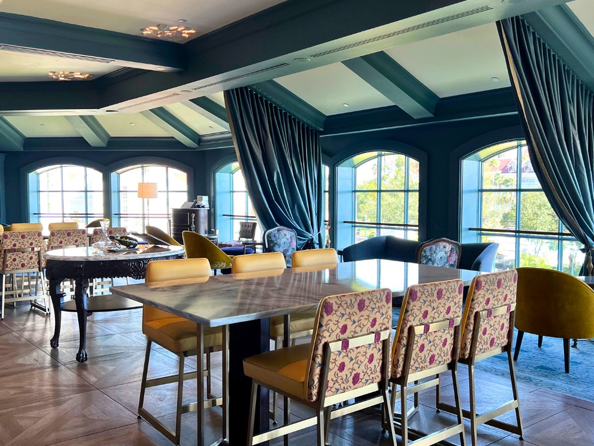 The Enchanted Rose lounge at Disney's Grand Floridian, marble-topped tables and floral high chairs under teal drapes, with arched windows onto the resort grounds