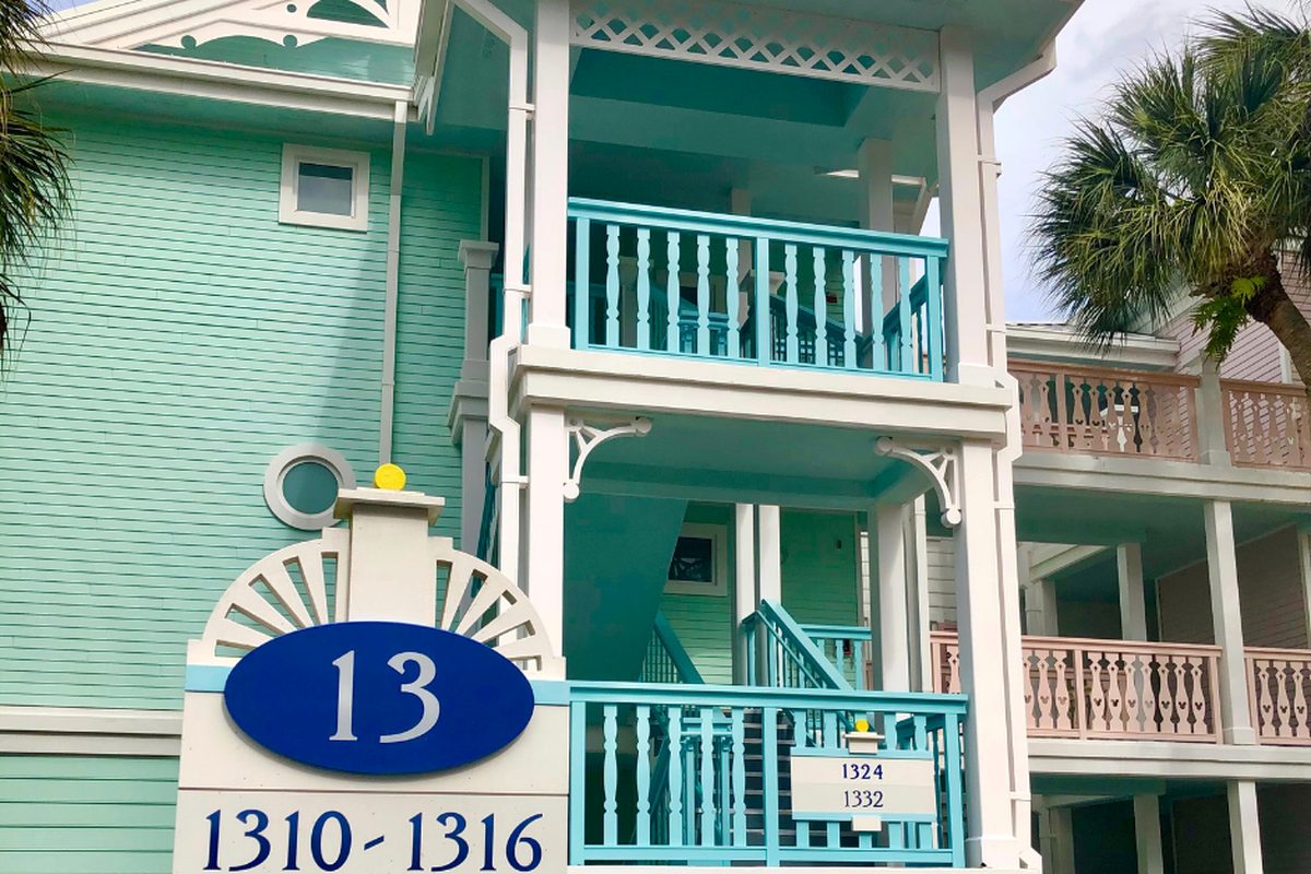 A pastel sea-green villa building at Disney's Old Key West Resort, with white gingerbread trim, turquoise balcony railings and the blue room-block sign for building 13