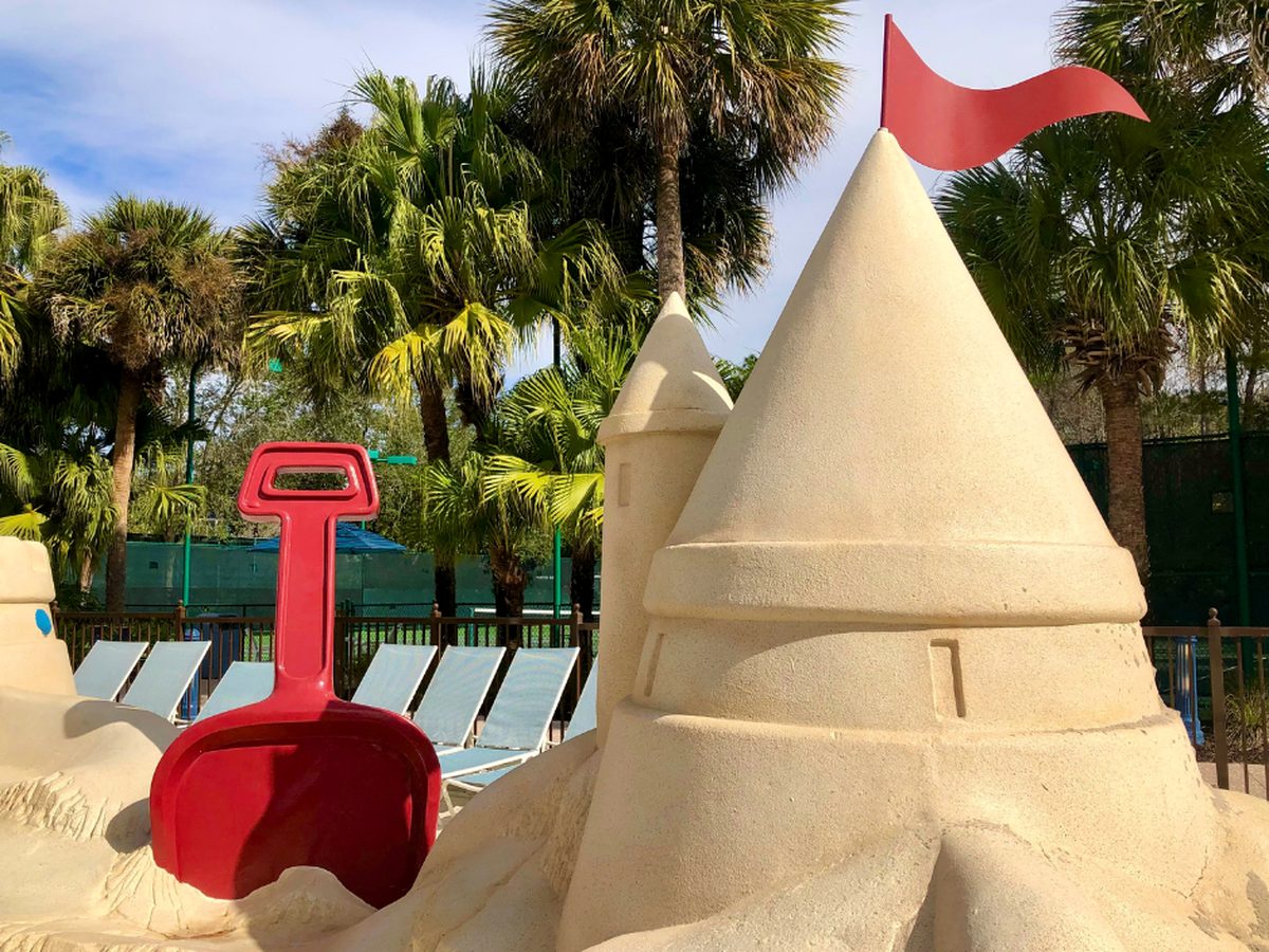 A giant model sandcastle with a red toy shovel beside sun loungers and palm trees at the Sandcastle Pool at Disney's Old Key West Resort