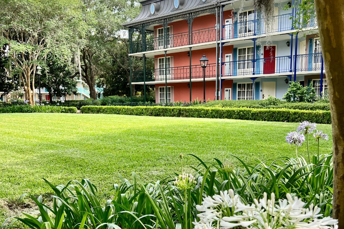 A pastel guest building at Disney's Port Orleans French Quarter with wrought-iron balconies, behind a lawn and agapanthus flowers