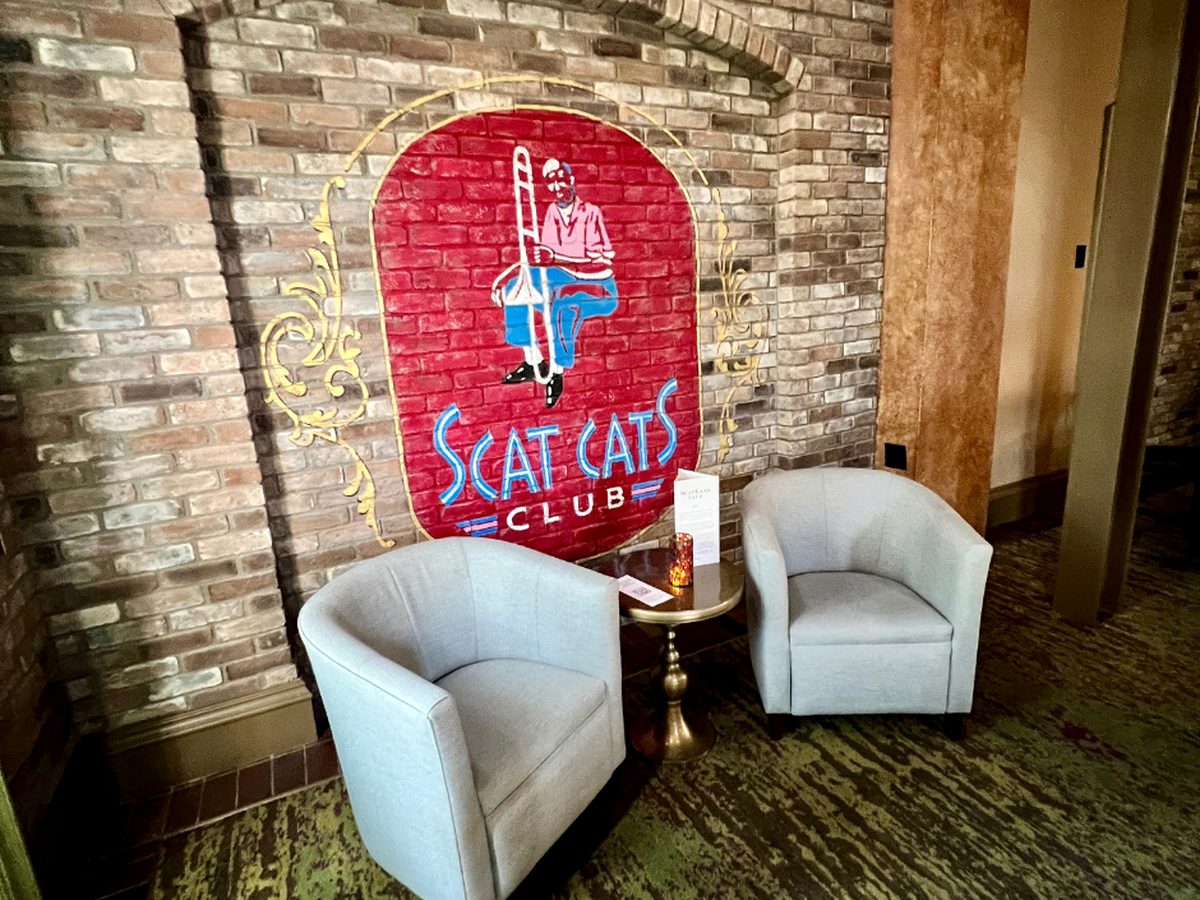The painted Scat Cat's Club sign on a brick wall behind two armchairs and a small table in the jazz lounge at Disney's Port Orleans French Quarter