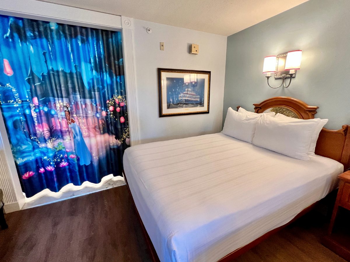 A queen bed at Disney's Port Orleans Riverside beside a full-length curtain printed with Tiana from The Princess and the Frog
