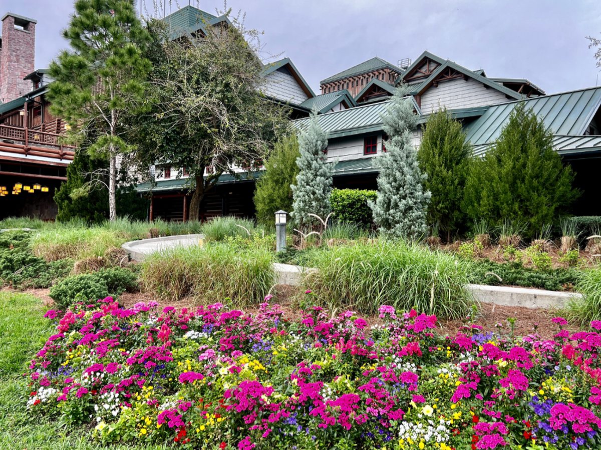 Pink, white and yellow flower beds in front of the green roofs and log walls of the main lodge at Disney's Wilderness Lodge
