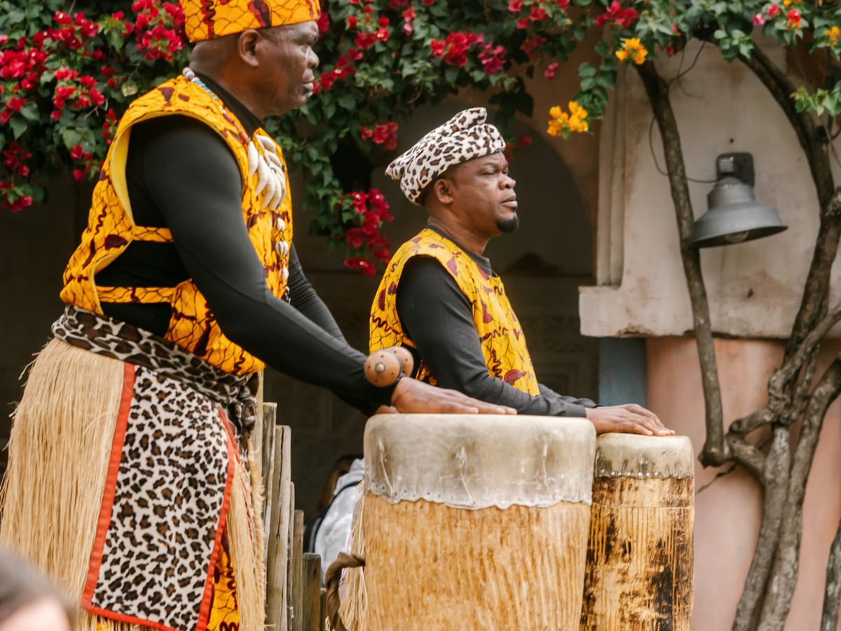 Two drummers in patterned costume with their tall drums in the Harambe village area of Animal Kingdom, bougainvillea behind them