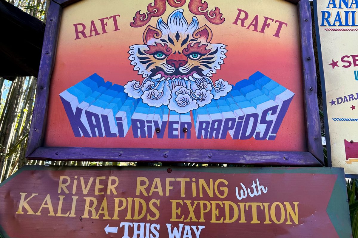 The carved and painted Kali River Rapids sign in the Asia area of Animal Kingdom, jungle planting around it