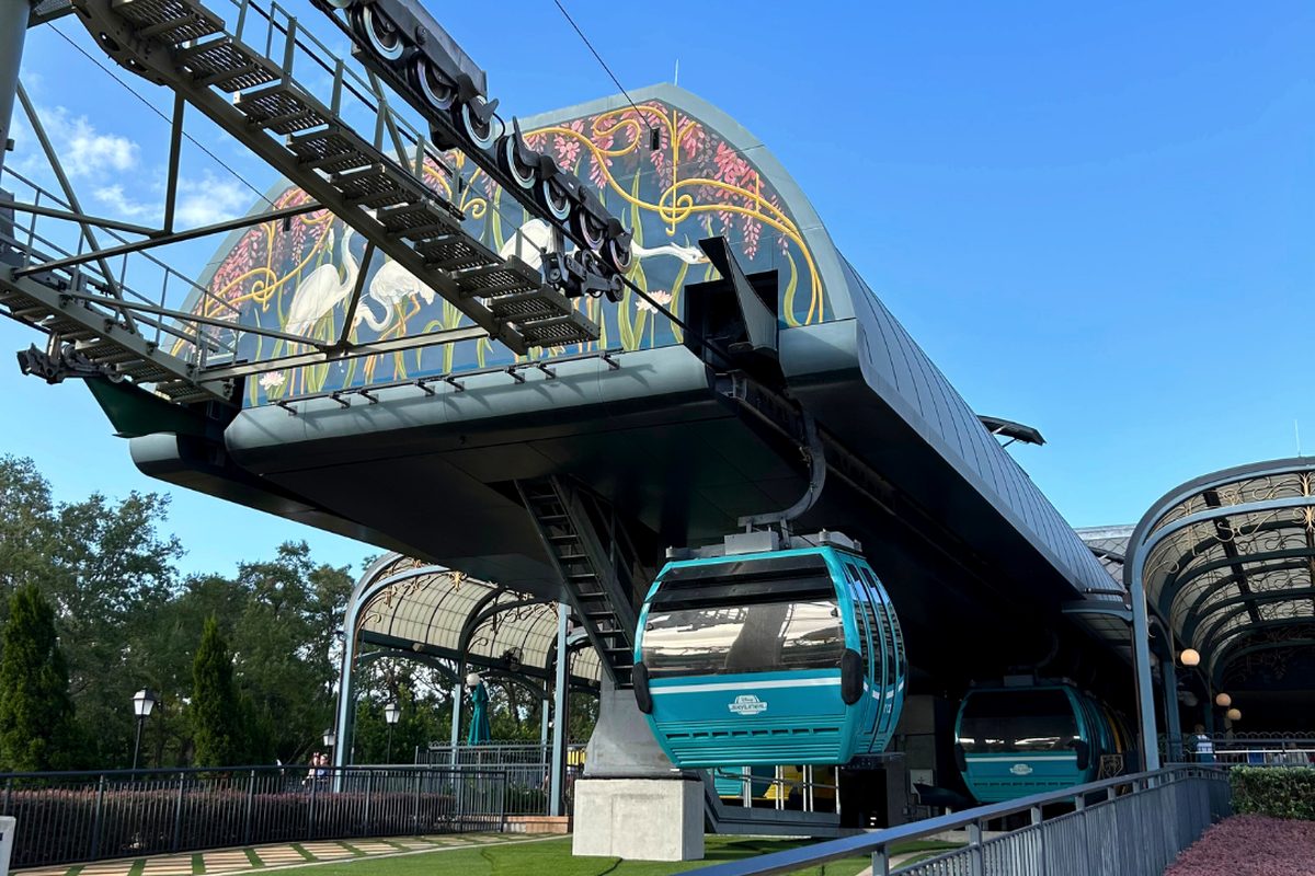 Turquoise Disney Skyliner gondolas arriving under the cables at the station beside the International Gateway