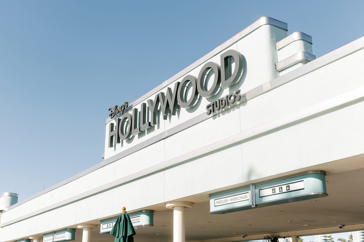 The Disney's Hollywood Studios sign in silver art-deco letters above the park entrance, against a clear blue sky