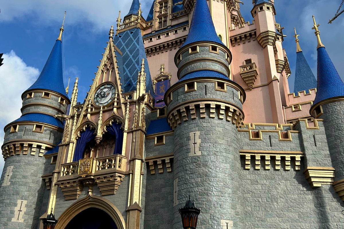 Cinderella Castle at Magic Kingdom, its grey stone base rising to pink walls and blue conical spires against a blue sky