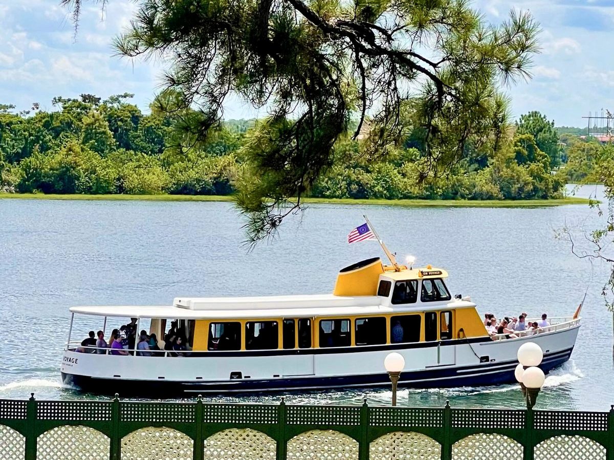 A yellow-and-white resort launch full of guests crossing the Seven Seas Lagoon on a sunny day