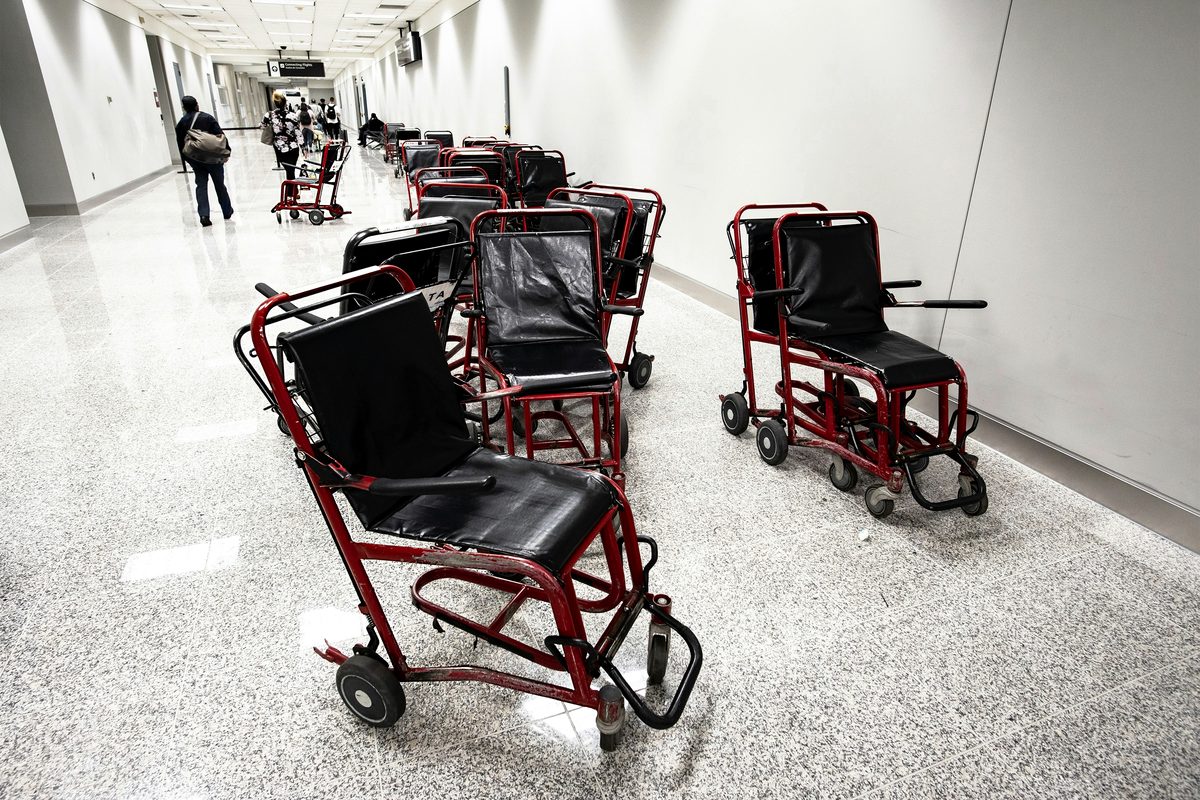 Empty red and black transport wheelchairs lined up in an airport corridor.