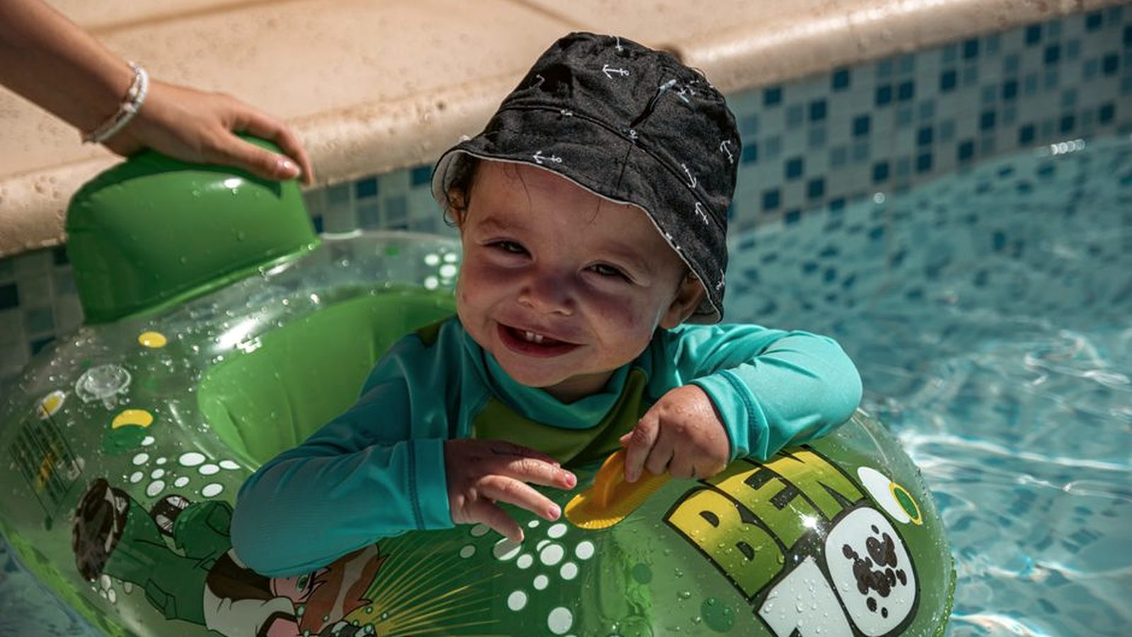 A toddler in a sun hat by a pool