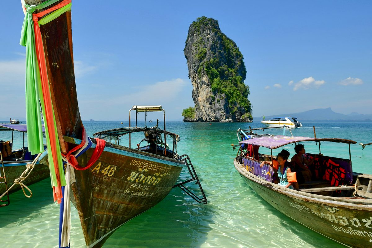 Wooden longtail boats on turquoise water beside a limestone island in Krabi.