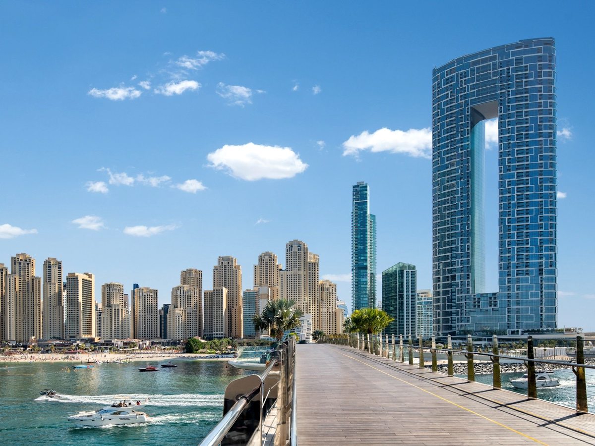 A wooden boardwalk and jetty reaching over the marina, with the resort tower and the Ain Dubai observation wheel behind.