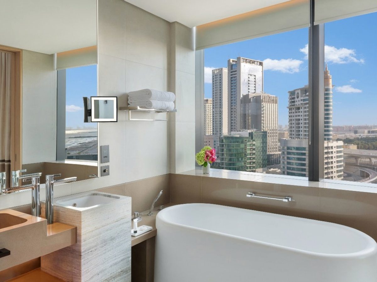 A marble bathroom with a freestanding oval bath by a floor-to-ceiling window looking to Ain Dubai, twin basins and a walk-in shower.