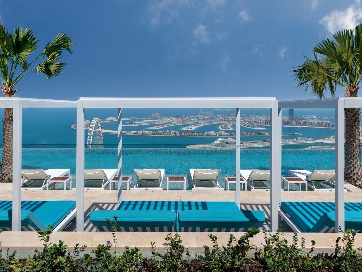 A row of white curtained cabana daybeds and sun loungers on a rooftop deck, looking over the sea towards the Palm and the Burj Al Arab.