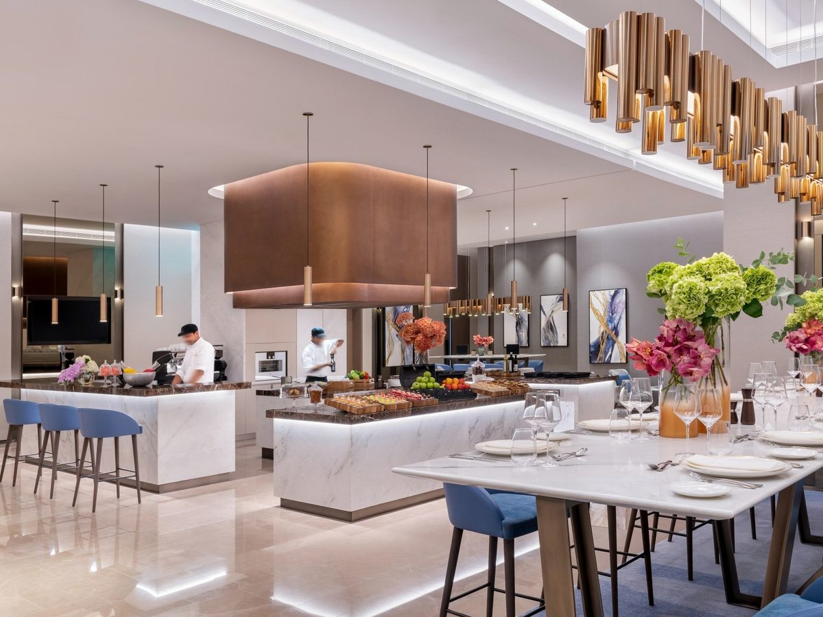 A generous breakfast buffet with live cooking stations, floral displays and chefs plating food under warm lighting.